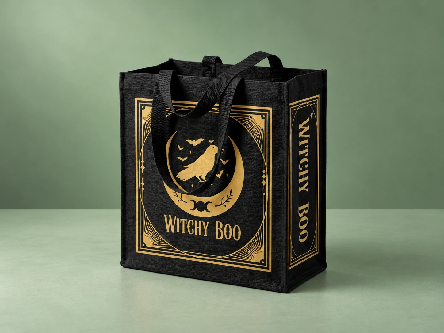 Witchy Boo black and gold bag, complete with handles, in a sage-green studio